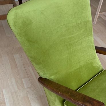 Green upholstered chair with wooden armrests on light wood floor.