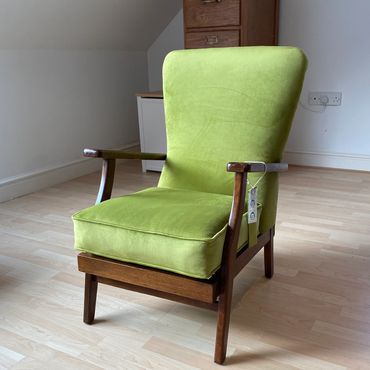 Bright green upholstered armchair with wooden frame on a light wooden floor.