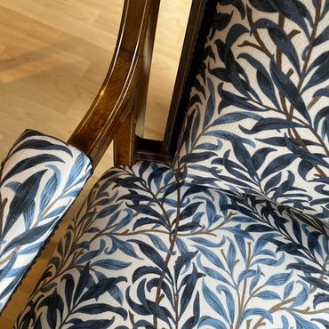 Close-up of a wooden chair with blue and white leaf patterned upholstery.