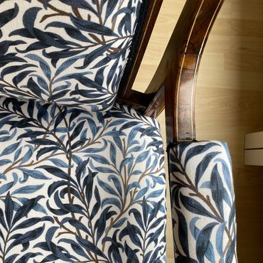 Close-up of a chair with blue and brown leafy patterned fabric and wooden frame.