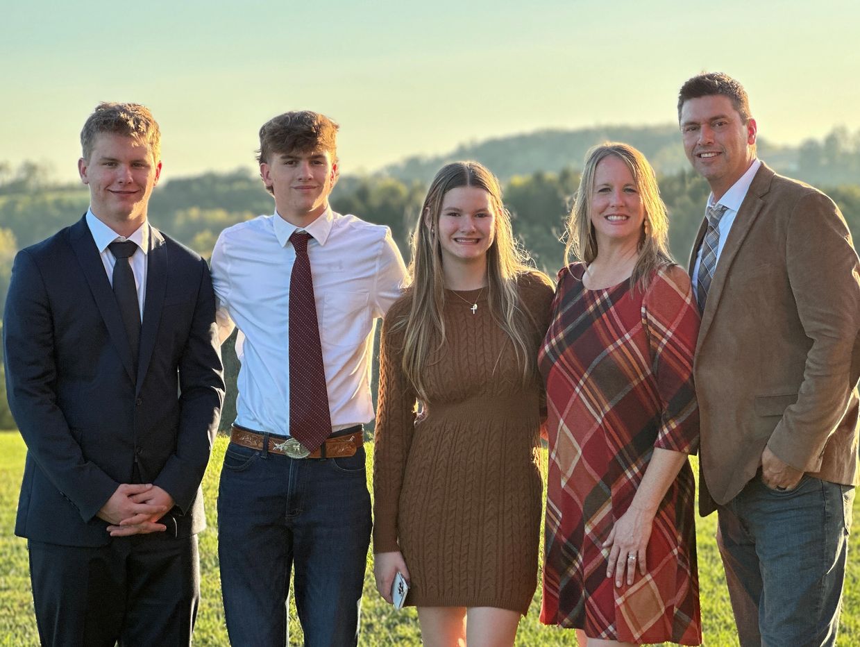 A well-dressed family standing outdoors with a scenic background at sunset.
