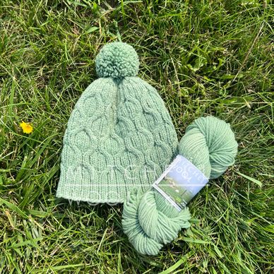 a hand knit green hat sits on a grassy field