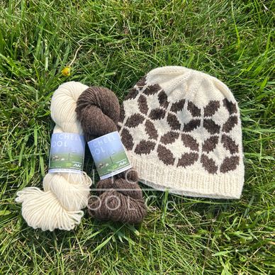 a white and brown hat with modern circles sits on green grass with two skeins of yarn