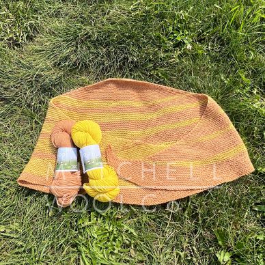 a yellow & orange hand knit shawl sits on green grass