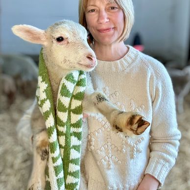 Sherry holds a lamb who is wearing a white and green handknit scarf