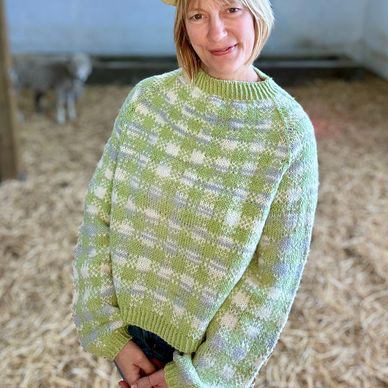 SHERRY WEARS AND OVERSIZED GREEN GINGHAM SWEATER IN THE BARN WITH A SHEEP IN THE BACKGROUND
