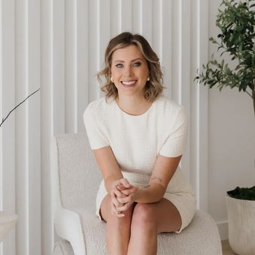 Smiling woman in white dress sitting on chair.