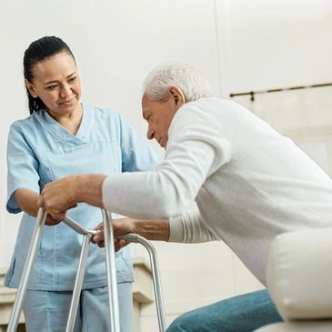 A nurse assists an elderly man using a walker indoors.