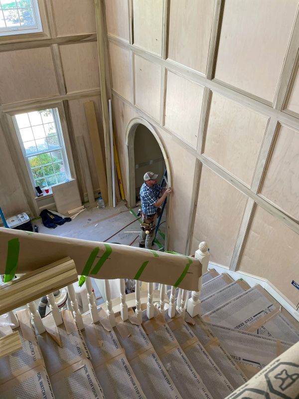 Worker installing wood paneling on walls near staircase.