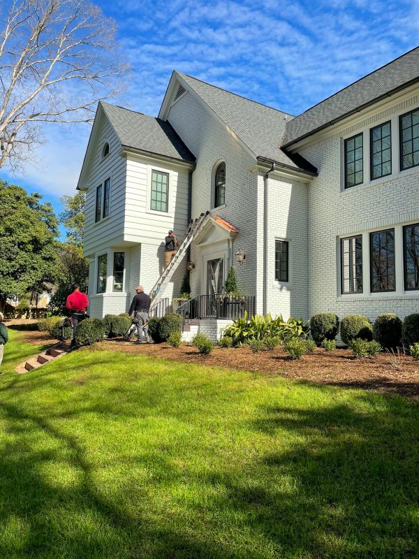 Workers on ladders repairing a large white brick house.
