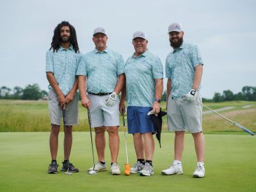 Four men standing on a golf course with clubs.