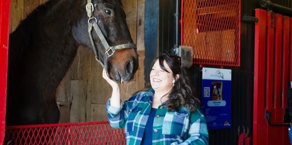 Woman smiling and touching a horse's face in a stable.
