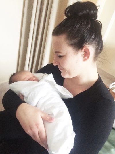 Woman lovingly holding a newborn baby wrapped in white.
