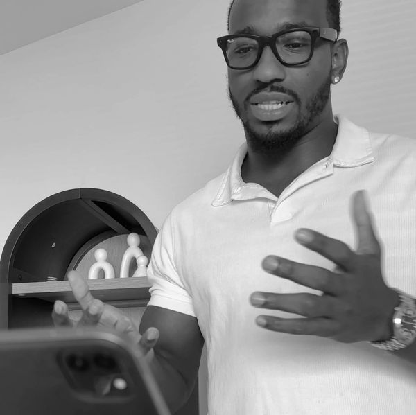 Man in glasses talking and gesturing with a phone in front of him.