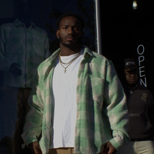 Man in a green checkered jacket standing in front of a store with an 'OPEN' sign.