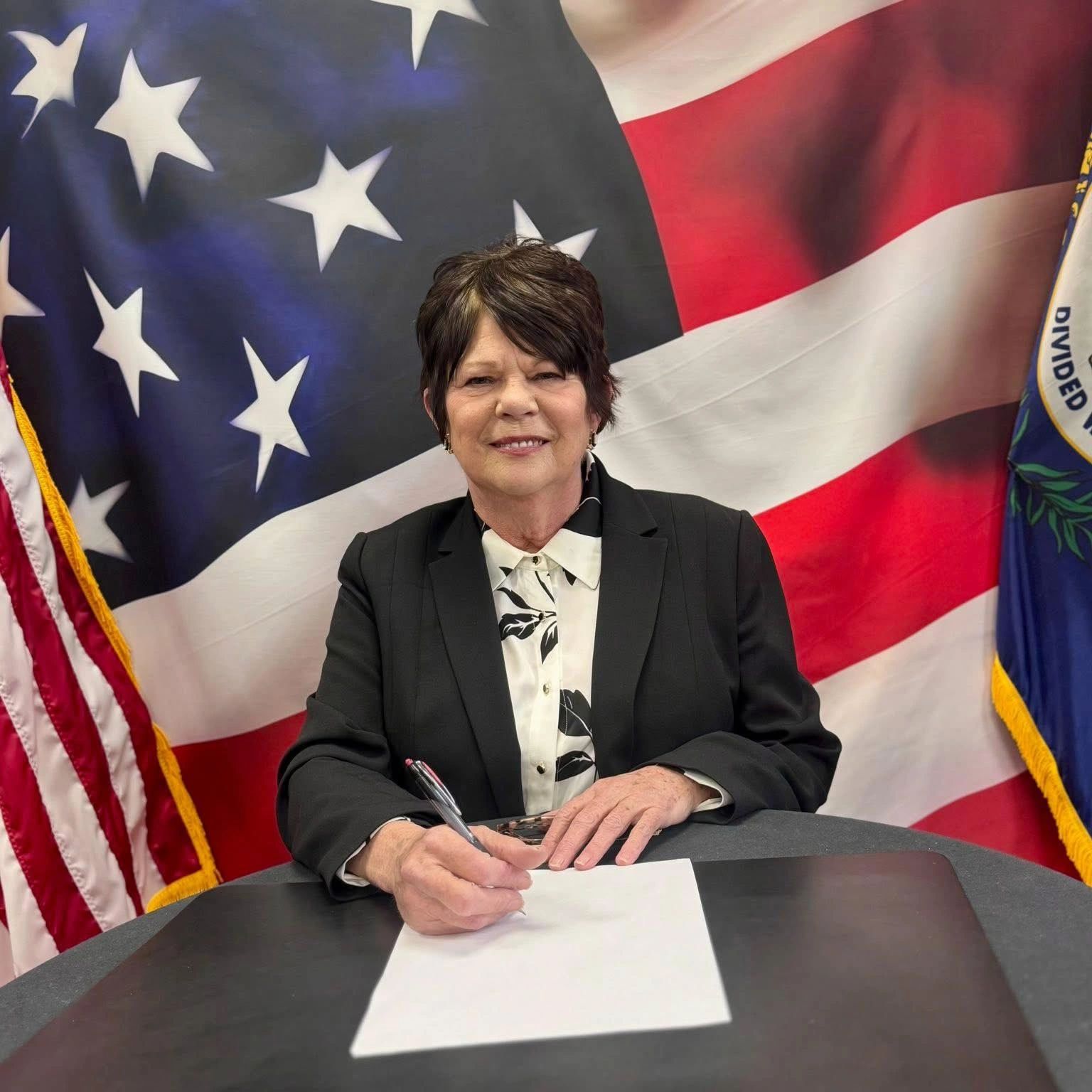 Woman signing a document with American flags in the background.