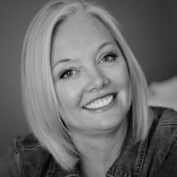 Smiling woman with straight blonde hair and denim jacket in black and white.