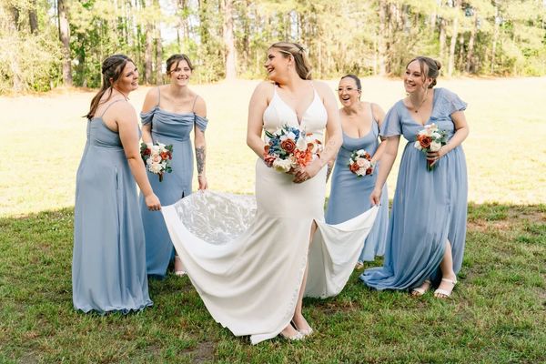 Bride in white gown with bridesmaids in blue dresses outdoors.