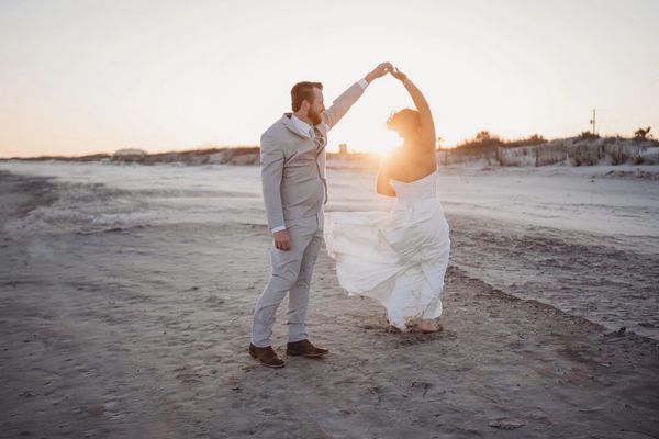 Couple dancing on the beach at sunset during their wedding.
