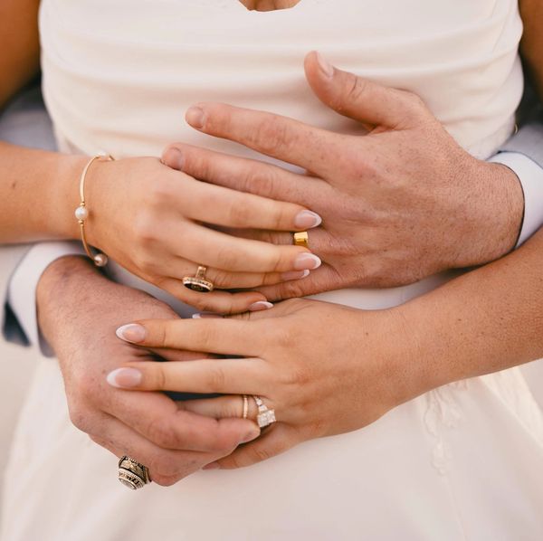 Close-up of intertwined hands with wedding rings and jewelry.