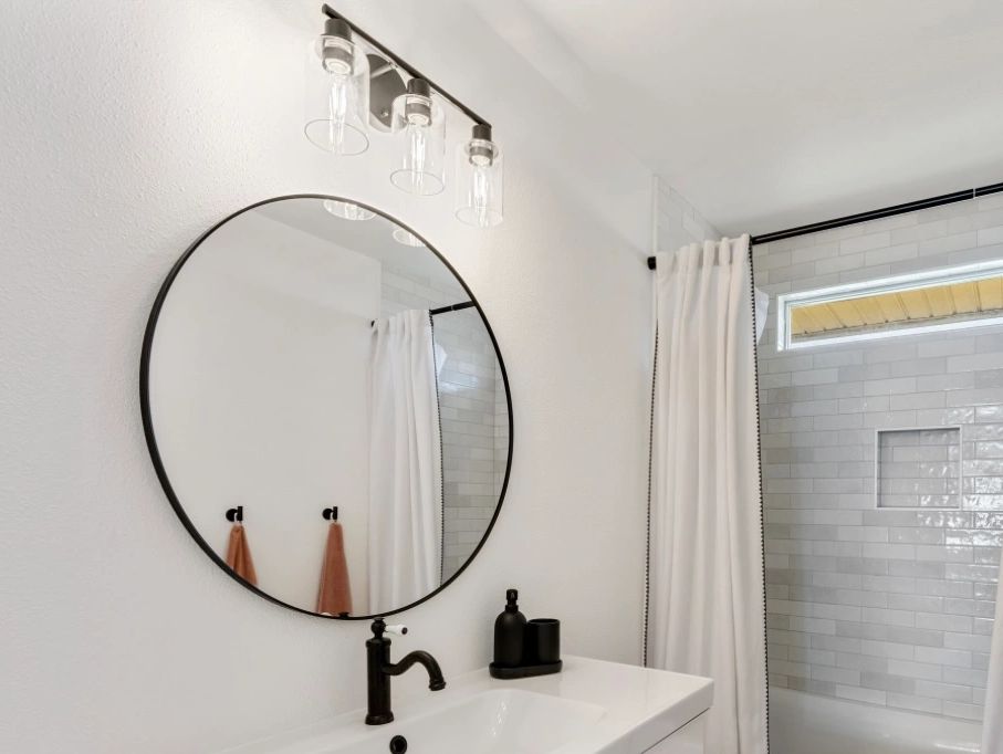 Minimalist white bathroom with black fixtures and a round mirror.