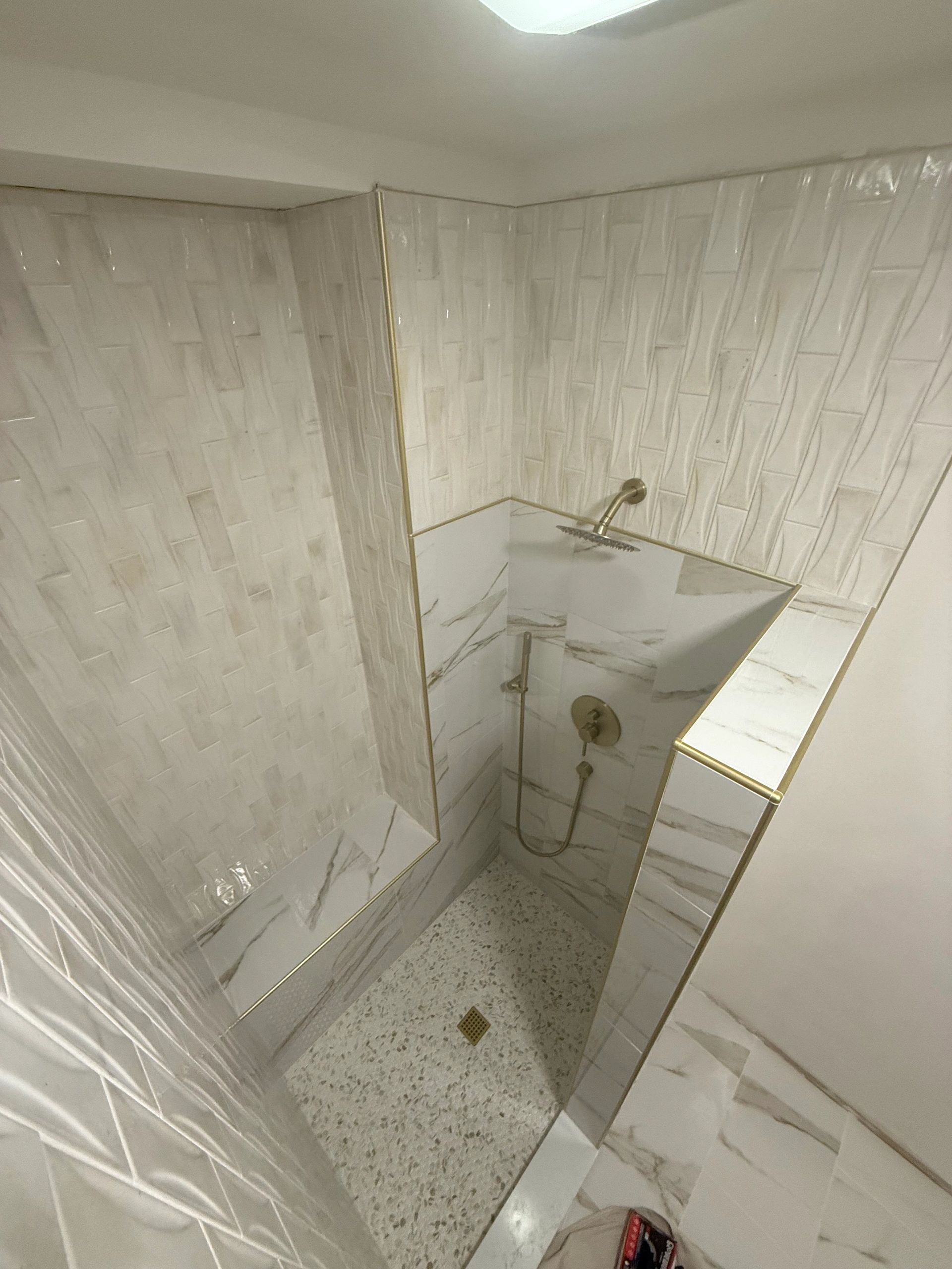 Modern shower with white tiles, gold trim, and terrazzo floor.