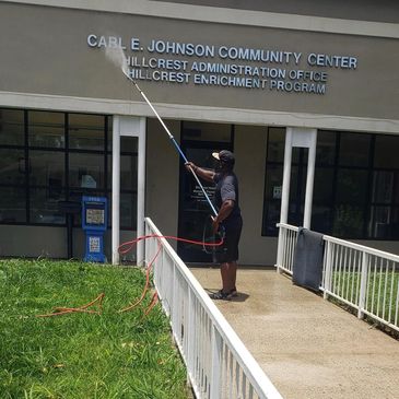 Man power washing the exterior of a community center on a sunny day.