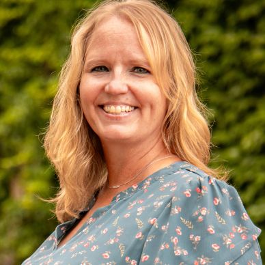 Smiling woman with blonde hair in floral dress outdoors.