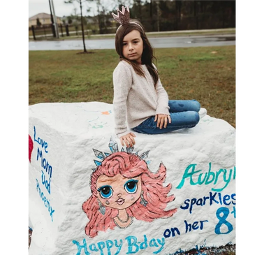 8 year old girl sitting on a custom hand-painted birthday rock painting