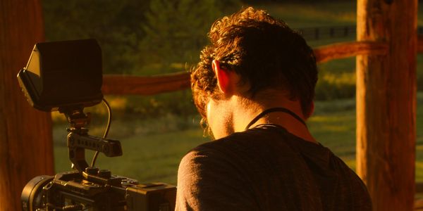 A person filming outdoors with professional camera in golden hour light.