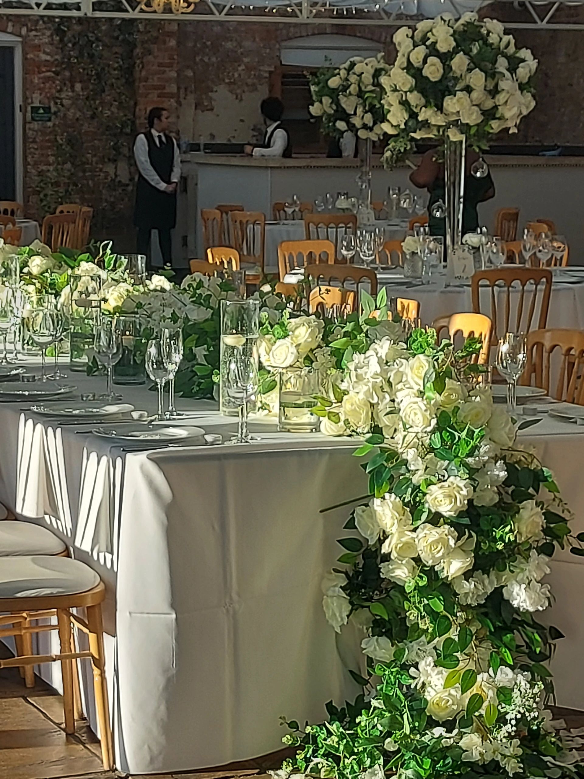 Elegant event setup with white floral arrangements and wooden chairs.