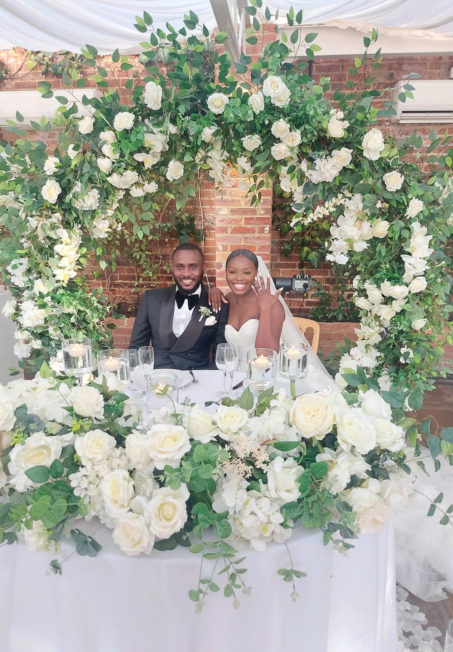 Happy newlywed couple smiling under floral arch.