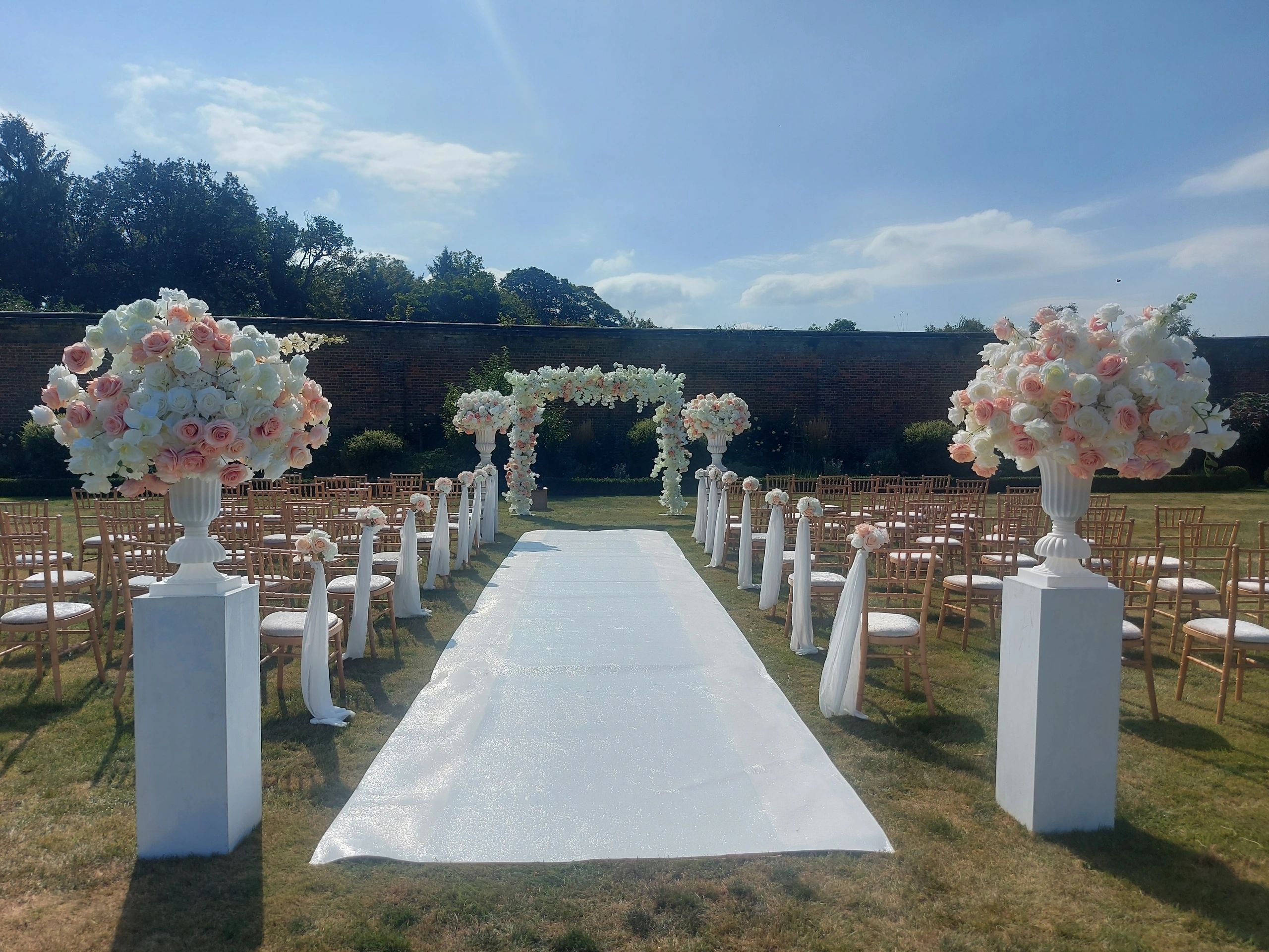 Outdoor wedding setup with white and pink floral decorations.
