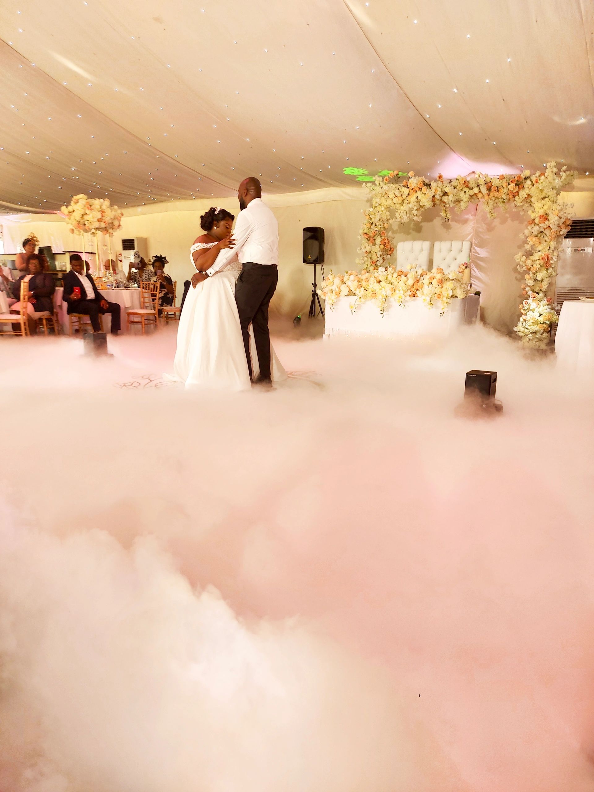 Couple dancing surrounded by fog at a decorated wedding venue.