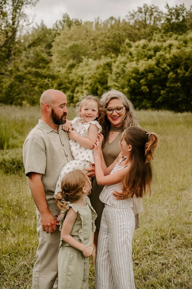 A happy family of five enjoying a moment outdoors in a grassy field.