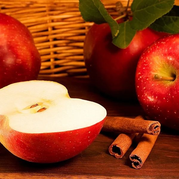 Red apples with cinnamon sticks on a wooden surface.