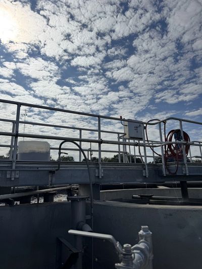 Industrial wastewater treatment plants with pipes and railings under a cloudy sky.