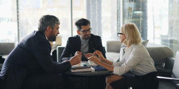 Three professionals engaged in a discussion around a table in a modern office.