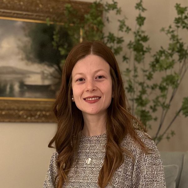 Smiling woman with long brown hair and pearl earrings indoors.
