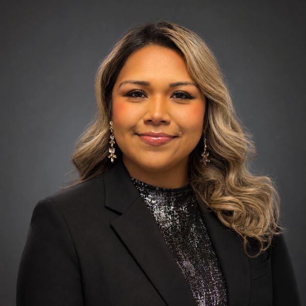 Smiling woman with wavy hair in black blazer and sequin top.