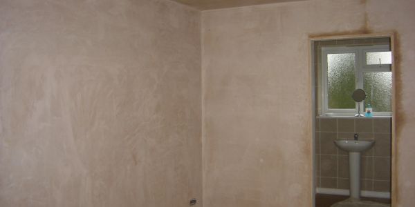 A room under renovation with freshly plastered walls and an adjoining bathroom.