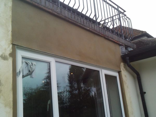 Freshly plastered wall above a sliding glass door with a metal railing above.