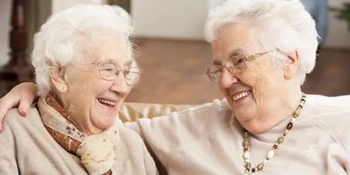 Two elderly women smiling warmly at each other, sharing a joyful moment.
