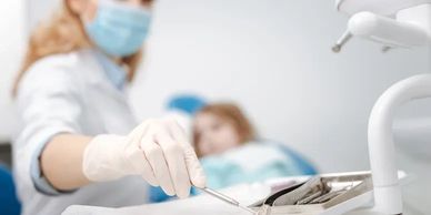 Dentist preparing tools for a dental procedure with patient in the background.