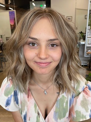 A woman is looking forward while getting a haircut in a salon.