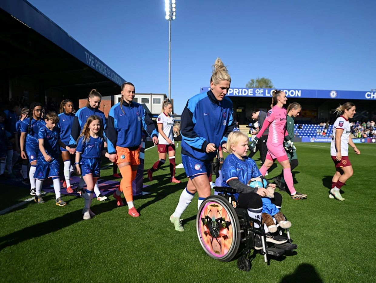 Chelsea Women's team walk out at Kingsmeadow. Millie's mascot is a young supporter in a wheelchair.