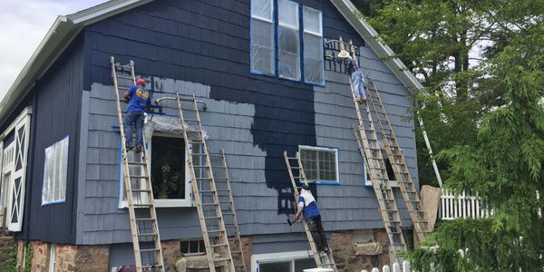 Three painters on ladders painting a house dark blue.