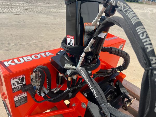 Close-up of Kubota machinery with hydraulic hoses and safety warnings.