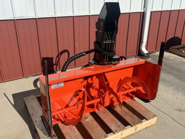 Bright orange Kubota BX2380 snowblower attachment on wooden pallet.