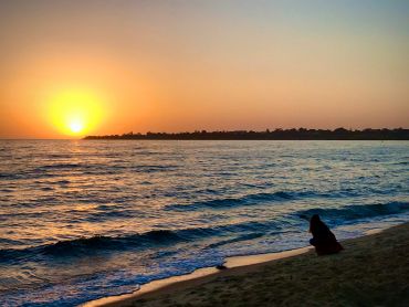 Sunset over the ocean with a person on the beach.